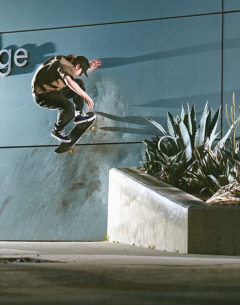 A skateboarder ollies onto the wall of a building in black and purple half cab shoes.