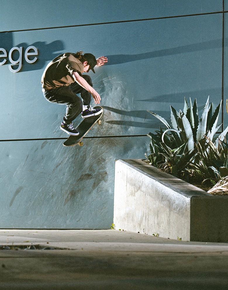 A skateboarder ollies onto the wall of a building in black and purple half cab shoes.