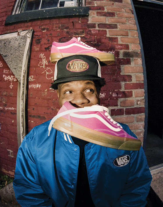 A member from the Hip-Hop/Rap band Hi-Tech behind a brick wall, Raspberry Pink Premium Old Skool shoes stacked on their head.