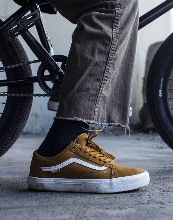 Close-up of a person wearing Golden Brown BMX Old Skool shoes, standing beside a BMX bike. 
