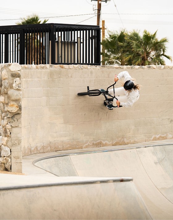 A full shot of a cyclist in protective gear performs a wall ride on a BMX bike at a skatepark. 