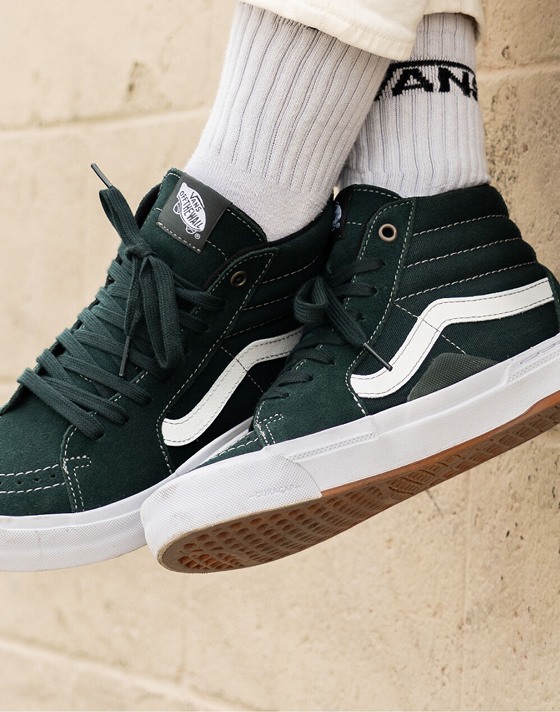 Close-up shot of a person wearing Dark Forest BMX Sk8-Hi shoes and white socks with a Vans logo. 