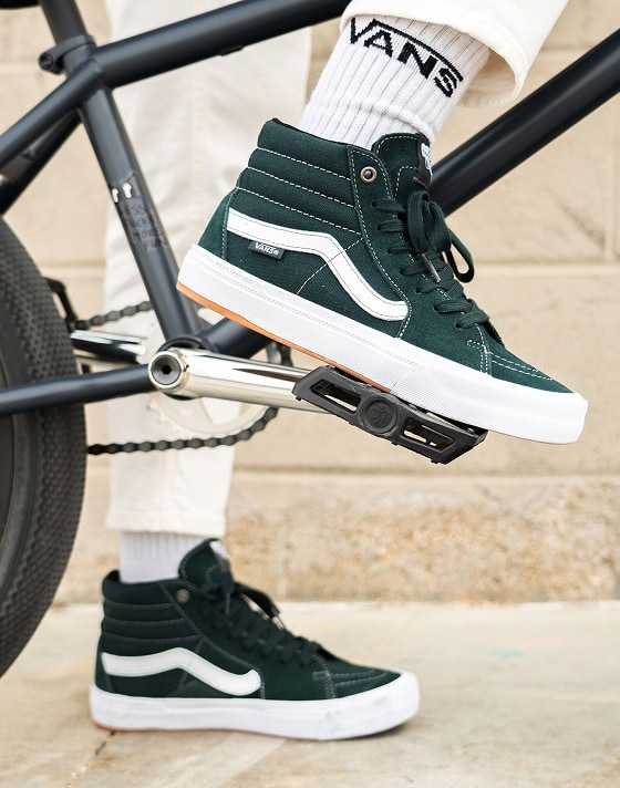 Close-up of a person wearing Dark Forest BMX Sk8-Hi shoes, standing beside a BMX bike.