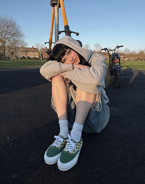 A man standing infront of an industrial building wearing a Vans green hat, tan pants and black authentic shoes.