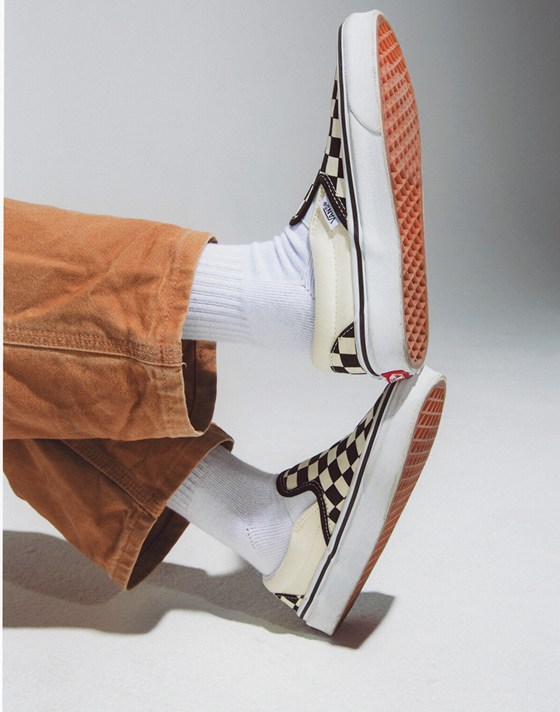 A kid kicks his feet up in black and white Checkerboard Classic Slip-On.