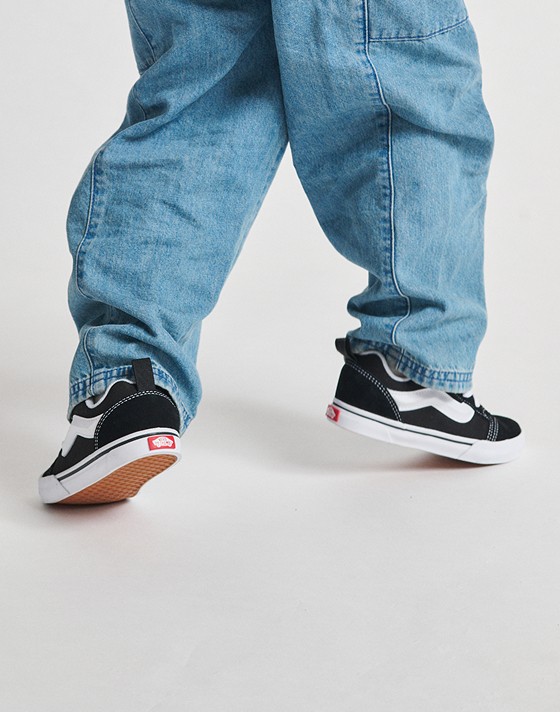 A kid walking in black and white Knu Skool with baggy blue jeans.