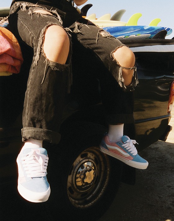 A waist-down shot of someone sitting in a truck bed wearing pink and blue Knu Skool at the beach.