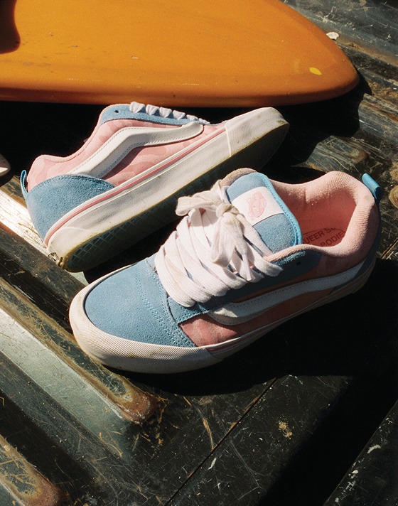 A pair of blue and pink Knu Skool rest on the bed of a truck next to a surfboard.