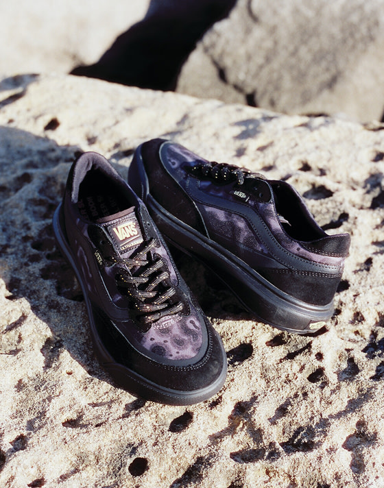 A pair of black and purple UltraRange 2.0 rest on a porous rock at the beach.