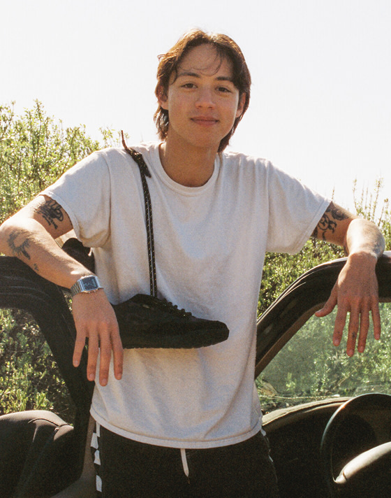 A person leans on a truck at the beach smiling for the camera with a pair of black UltraRange2.0 slung over their shoulder.