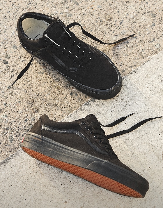 A pair of black Old Skool shoes laying on the cement. 
