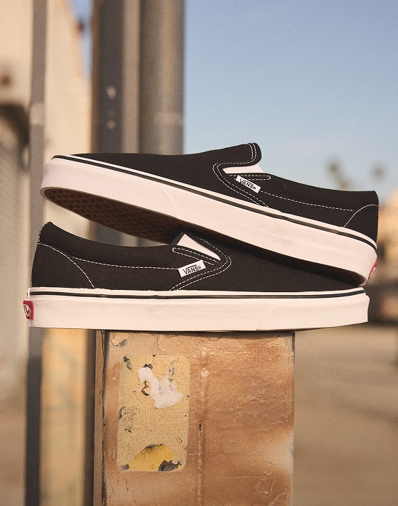 Two black and white Classic Slip-On are stacked on top of each other on top of a metal pole in an urban setting.