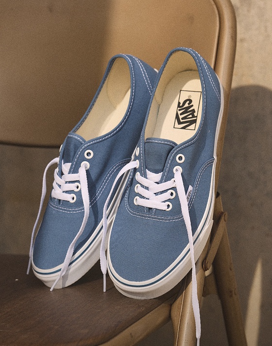Two blue and white Authentic rest on the back of a folding chair with their laces hanging down.