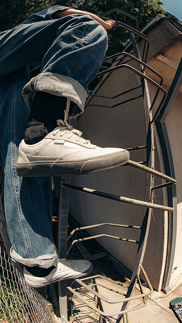 A woman climbs a ladder-like structure to the roof of a building wearing gray Curren shoes.