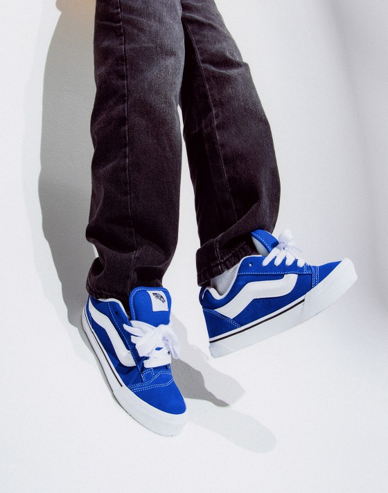 A close-up of a boy jumping wearing dark jeans and blue Knu Skool shoes.