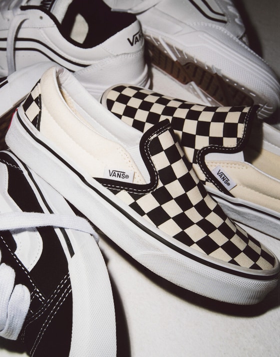 Close-up of a pair of black and white Checkerboard Slip-On among other Vans shoes.