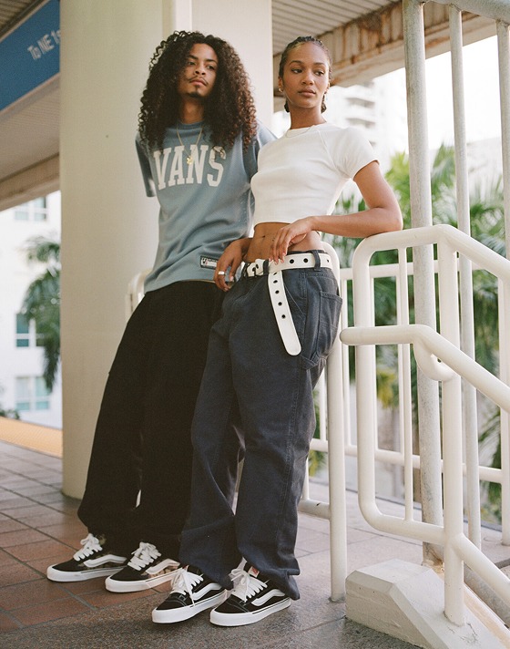 A man and woman lean on the white handrail in a train station wearing Vans clothes and Knu Skool shoes.