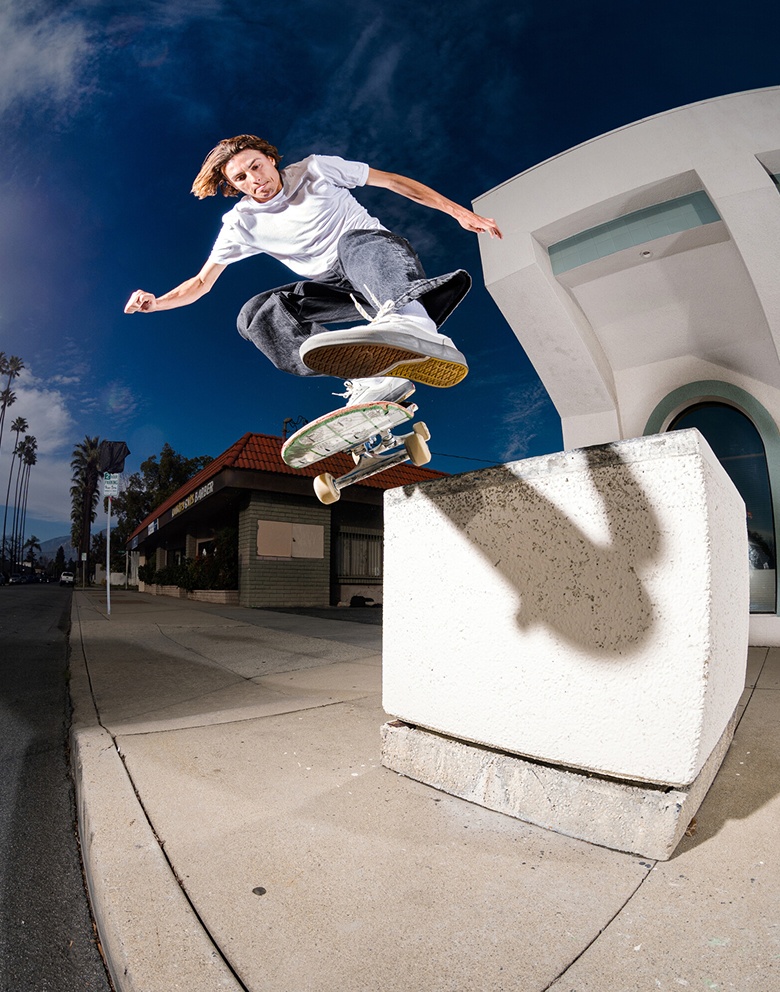 Vans skateboarder Curren Caples does a trick in the air wearing a white t-shirt, black jeans, and white Curren shoes.