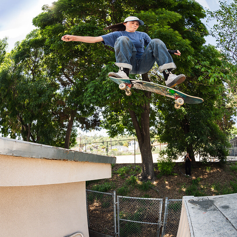 A man pushes off the ground skating, his back foot towards the camera wearing green and blue Half Cab.