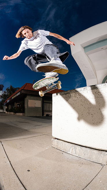 Vans skateboarder Curren Caples does a trick in the air wearing a white t-shirt, black jeans, and white Curren shoes.