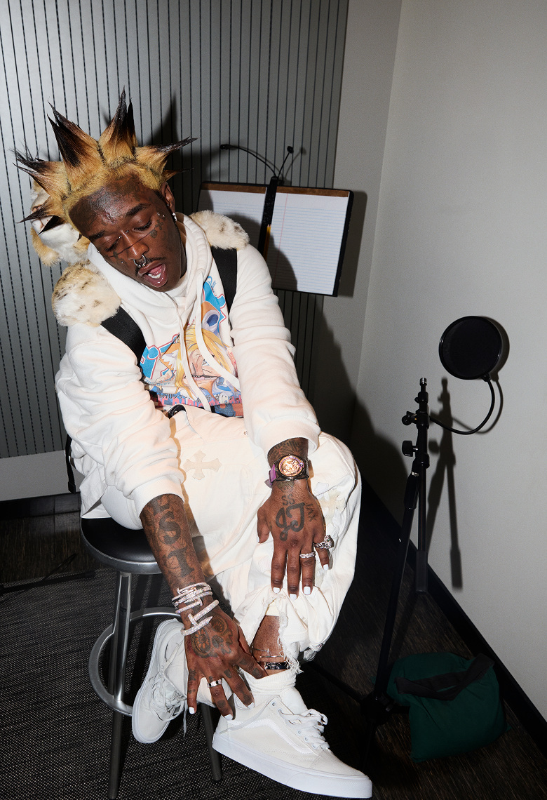 Lil Uzi Vert wears white pants and a white hoodie, showing a silver anklet over his white Old Skool shoes in his studio.