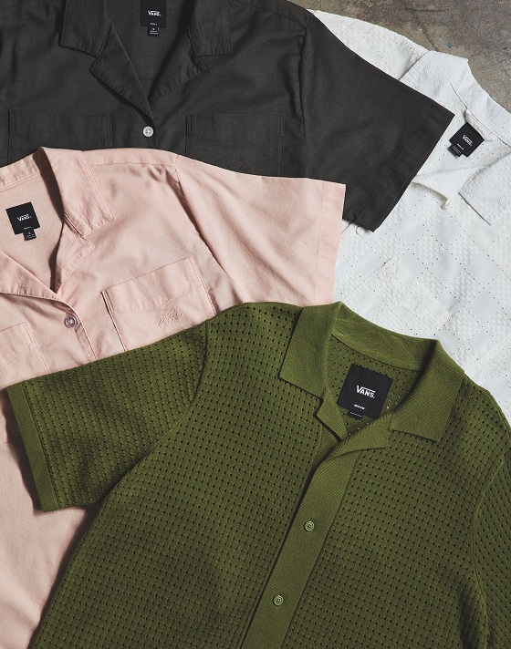 A bunch of Vans shirts lay flat on the ground showing a variety of colors, from green to white to pink to black to white.