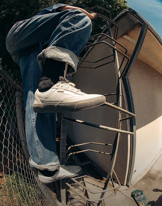 A skater with rolled up jeans climbs a ladder to a roof wearing gray Curren shoes.