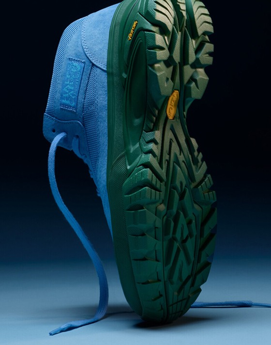 A close-up shot of a OTW Half Cab 33 Trail Vibram sneaker standing on its toe. The shoe stands on a white studio background with low light, and the background fades into black.