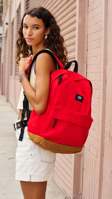 A young woman looks over her shoulder at the camera wearing the Everydayness Crop Tank Top and red Old Skool Sport Backpack.
