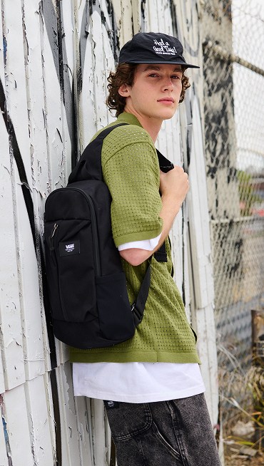 A young man looks over his shoulder at the camera in the Feldman Sweater Shirt, Drill Chore Loose Denim 22-inch Shorts, and Warp Ripstop Sling Bag.