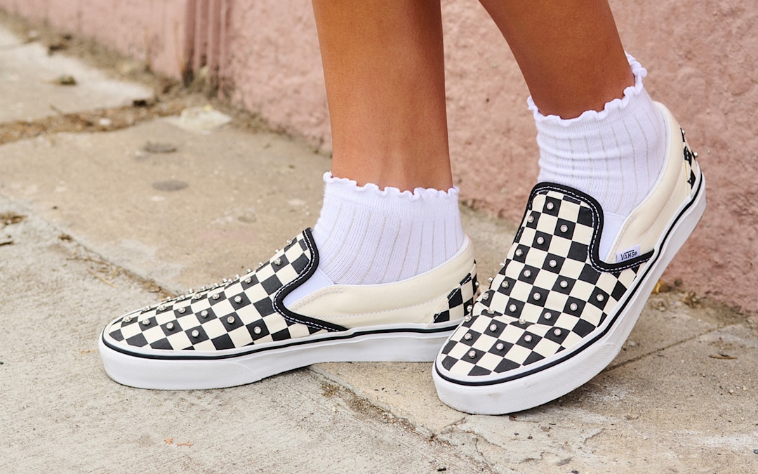 A close-up of a girl wearing rhinestone-embedded black and white Checkerboard Classic Slip-On.