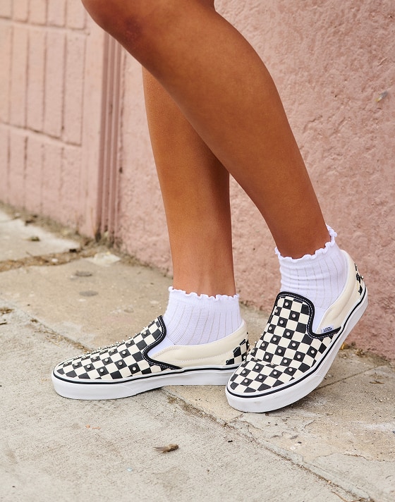 A close-up of a girl wearing rhinestone-embedded black and white Checkerboard Classic Slip-On.