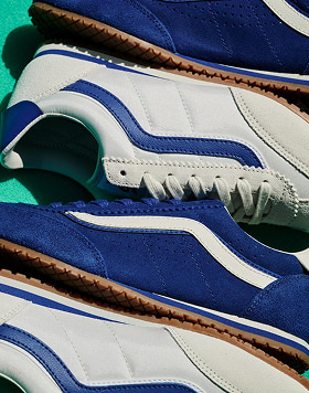 Close-up of two pairs of Vans Super Lowpro sneakers with white and blue suede uppers, brown rubber soles, and white midsoles.