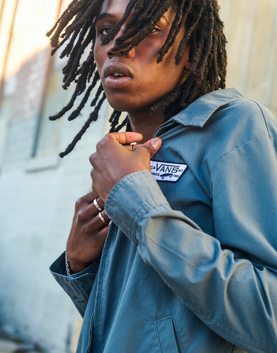 Close up of a man posing outside in a green Vans jacket.