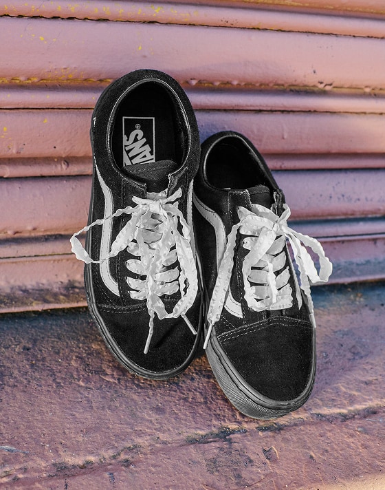 Black Vans Old Skool shoes lean against a dusty rose warehouse wall.