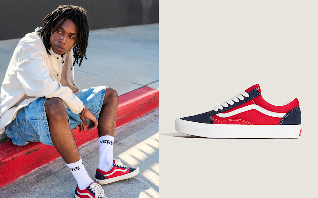 A man sits on a curb wearing red Old Skool shoes.