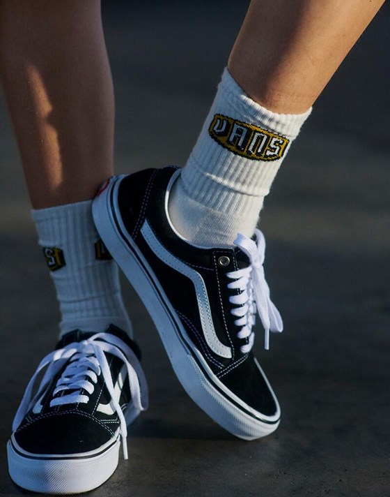A close-up of someone wearing white Vans crew socks and black and white Old Skool.
