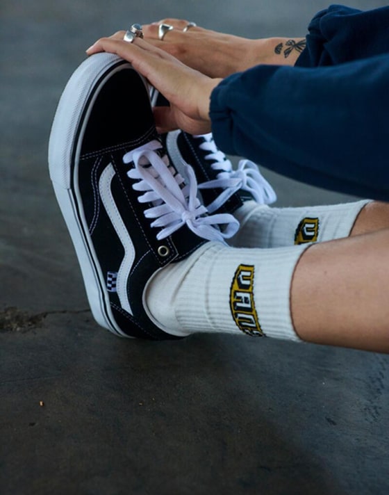 A person stretches and touches their toes in white Vans crew socks and black and white Old Skool.