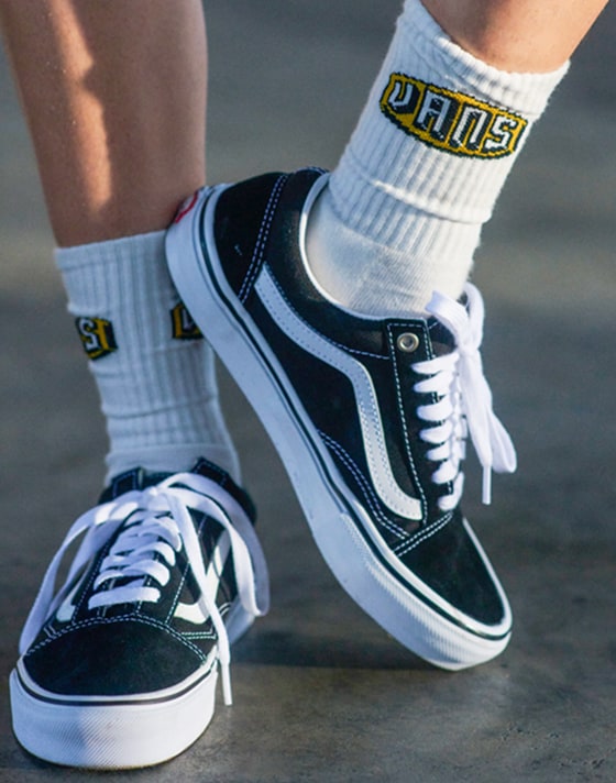 A close-up of someone wearing white Vans crew socks and black and white Old Skool.