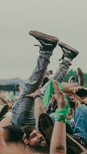 A person crowd surfs with their legs straight in the air wearing black and white Sk8-Hi at Warped Tour.