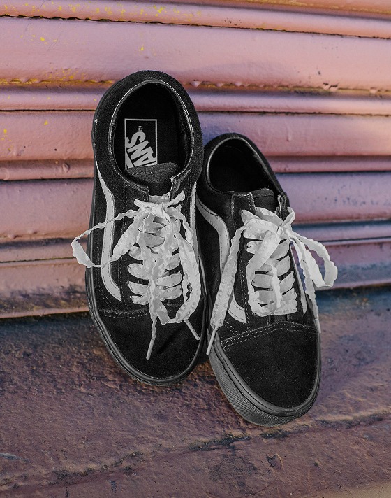 A pair of black and white old Skool lean up against a sliding garage door with their laces done.
