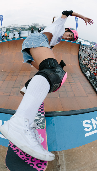 A Vans skater catches the edge of a halfpipe in white Sk8-Hi shoes before dropping in again.
