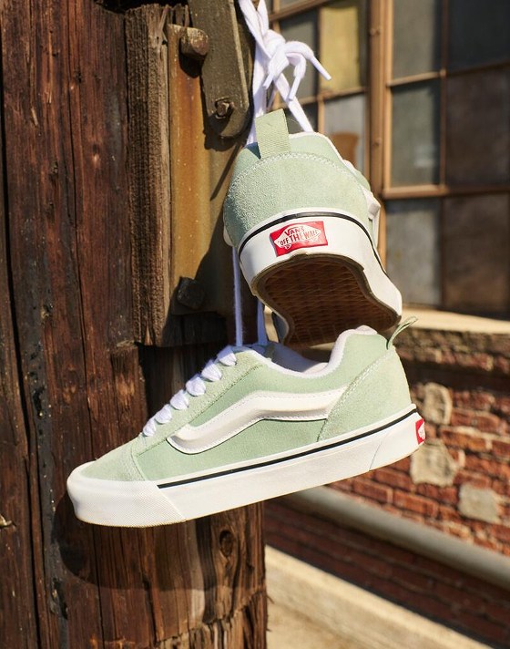 A pair of grey mint green Knu Skool hang from a nail by their laces in the afternoon sun.