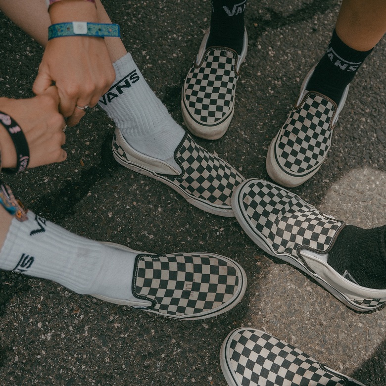 Close-up of three friends wearing black and white Checkerboard Classic Slip-On sitting in a circle.
