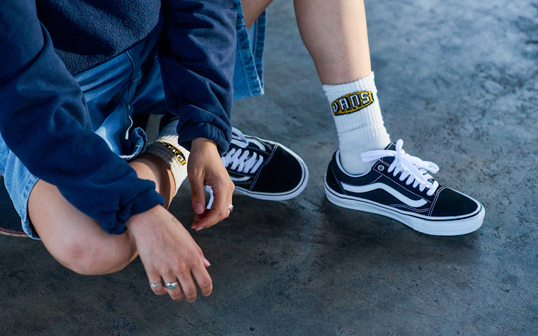 A person sits on the concrete wearing denim shorts, Vans quarter socks, and black and white Old Skool.