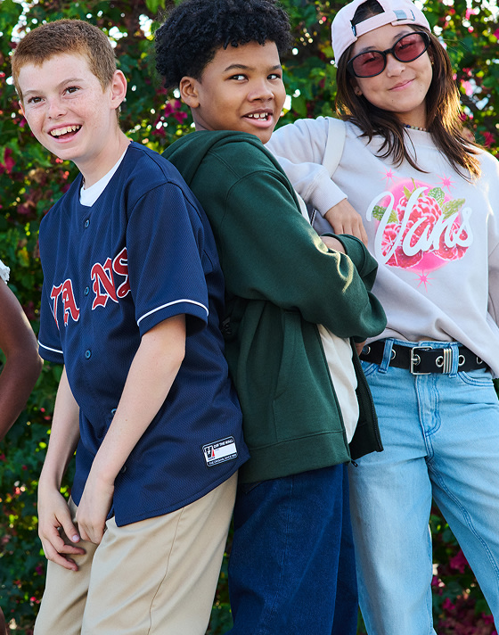 Three kids smile and pose for the camera in Vans clothes.