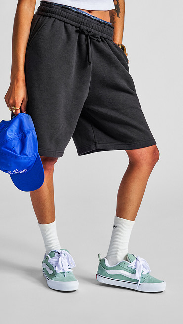 A chest-down shot of someone posing in mint Knu Skool shoes while wearing baggy black sweatshorts and white crew socks.