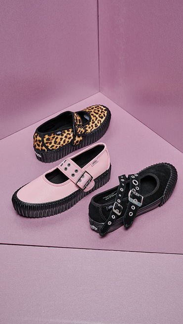 A black Mary Jane, a leopard Mary Jane Creeper Shoe, and a pink Mary Jane Creeper Shoe are laid out on a pink floor and backdrop.