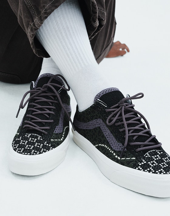 A knee-down shot of someone wearing Cheetah Dried Kelp Green Premium Old Skool paired with white crew socks and dark pants.