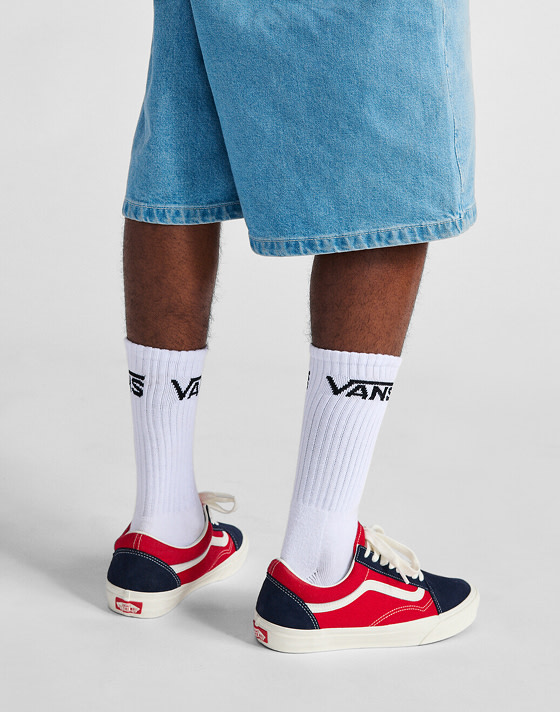 A waist-down shot of a man wearing red and navy Old Skool paired with blue denim shorts.